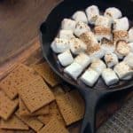 marshmallows over melted chocolate in a cast iron skillet with a side of graham crackers