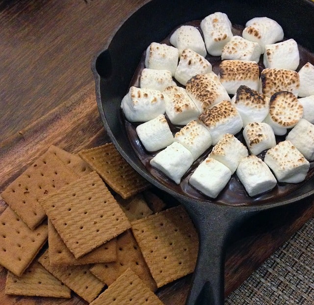 marshmallows over melted chocolate in a cast iron skillet with a side of graham crackers