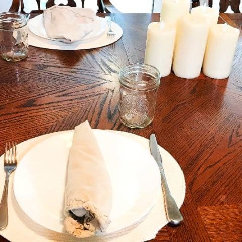 Table setting of plates, napkins, silverware and candles with cotton rope placemats.